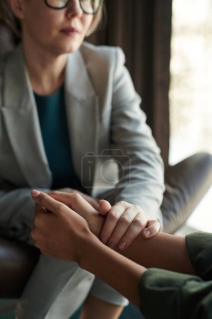 Photo for Close-up of experienced psychologist keeping hand on those of young depressed female patient while comforting her during session - Royalty Free Image