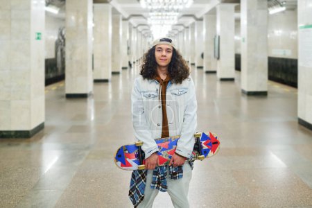 Photo for Happy teenage boy in denim casualwear looking at camera while standing against long tunnel of metro station and waiting for subway train - Royalty Free Image