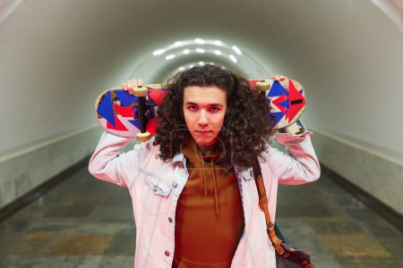 Photo for Serious teenage guy in casualwear holding skateboard behind his head while standing in front of camera against tunnel in subway station - Royalty Free Image