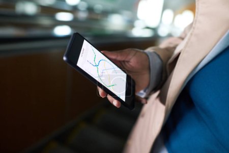 Foto de Primer plano del teléfono inteligente con mapa de ruta del metro en pantalla en la mano de la joven afroamericana con jersey azul y gabardina beige - Imagen libre de derechos
