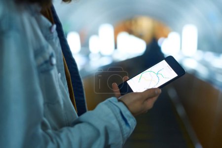 Photo for Close-up of boy in blue denim jacket holding smartphone with metro route map on screen while standing on escalator and moving downwards - Royalty Free Image