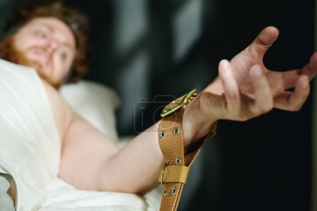 Photo for Focus on hand of aggressive male patient of mental hospital bound with tight brown belt during epileptic or hysteria seizure or panic attack - Royalty Free Image