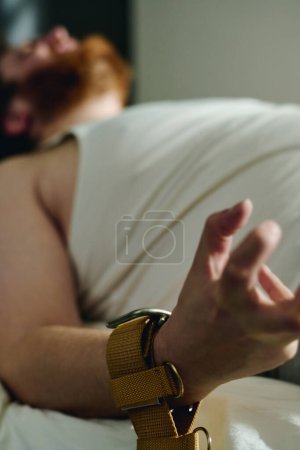 Téléchargez les photos : Concentrez-vous sur la main liée d'un jeune homme agressif souffrant d'hystérie ou d'un autre problème psychiatrique couché sur le lit pendant la thérapie clinique - en image libre de droit