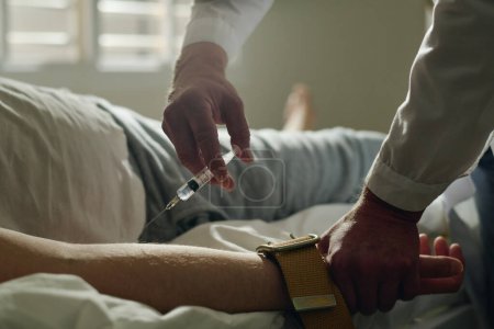 Nahaufnahme eines Arztes der Irrenanstalt, der einem jungen männlichen Patienten mit saisonaler affektiver Störung eine Spritze verabreicht, der auf der Krankenhausstation im Bett liegt