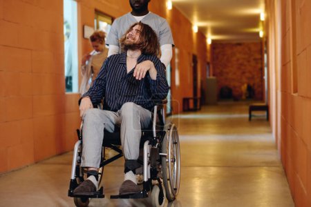 Photo for Cropped shot of African American male assistant pushing wheelchair with insane patient suffering from seasonal affective disorder - Royalty Free Image