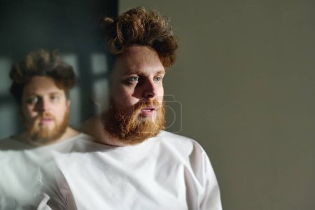 Photo for Young bearded insane male patient of mental clinics in straitjacket standing in front of camera in hospital ward during therapy - Royalty Free Image