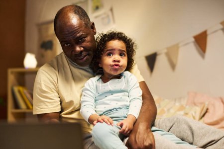 Photo for African American dad using laptop while playing with his child in bedroom - Royalty Free Image
