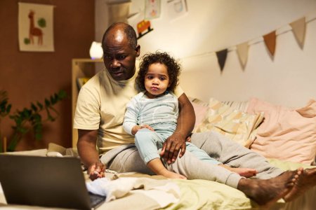 Photo for African American dad working online on laptop while sitting with baby at home - Royalty Free Image