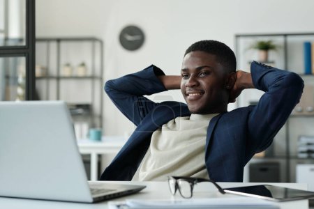 Foto de Joven hombre de negocios descansado manteniendo las manos detrás de la cabeza y mirando la pantalla del ordenador portátil mientras ve video en línea y disfruta del descanso - Imagen libre de derechos
