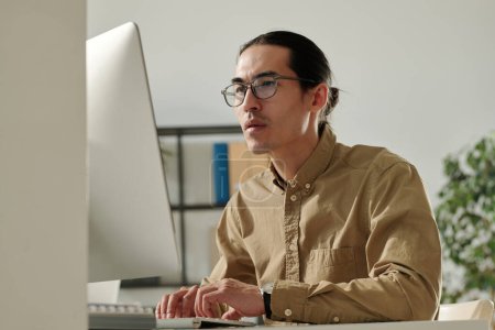 Foto de Joven emprendedor asiático que mira los datos financieros en línea en la pantalla del ordenador mientras lo analiza y prepara el informe para el seminario - Imagen libre de derechos