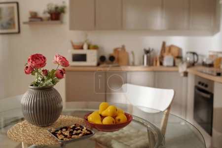 Téléchargez les photos : Plusieurs poires jaunes sur plaque, noix et vase avec bouquet de fleurs rouges sur table ronde en verre debout au centre de la cuisine spacieuse - en image libre de droit