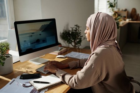 Foto de Diseñadora web femenina creativa joven sentada en el lugar de trabajo frente al monitor de la computadora y escribiendo mientras trabaja en un nuevo sitio web - Imagen libre de derechos