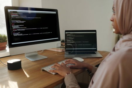 Téléchargez les photos : Concentrez-vous sur les mains d'une jeune programmeuse musulmane décodant des données ou développant de nouveaux logiciels alors qu'elle est assise devant un écran d'ordinateur - en image libre de droit
