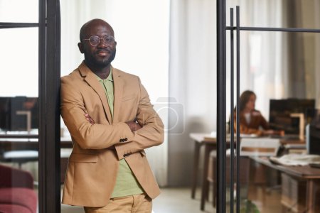 Photo for Young confident businessman in formalwear standing in door of coworking area against his colleague sitting by workplace in front of computer - Royalty Free Image