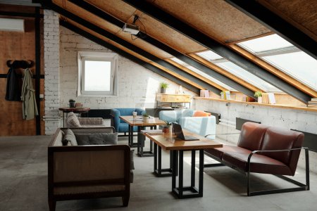 Photo for Interior of spacious loft studio or coworking space with tables in the center surrounded by several stylish and comfortable couches and armchair - Royalty Free Image