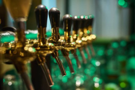 Téléchargez les photos : Focus sur l'un des robinets de bière métalliques dans la rangée de robinets avec interrupteurs noirs debout sur le comptoir du bar dans un grand pub ou restaurant moderne - en image libre de droit