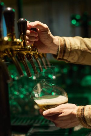 Foto de Manos del joven barman cambiando el grifo y vertiendo cerveza sin filtrar en un vaso antes de servirla al cliente del bar, pub o restaurante - Imagen libre de derechos