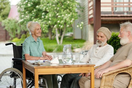 Photo for Group of senior people sitting by table with jug of water and medical stuff and discussing their health problems while waiting for nurse - Royalty Free Image