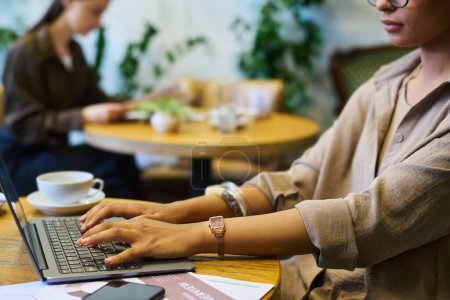 Téléchargez les photos : Mains de la jeune femme d'affaires afro-américaine sur clavier portable tapant alors qu'elle était assise à table dans un café ou un espace de coworking pendant le réseau - en image libre de droit