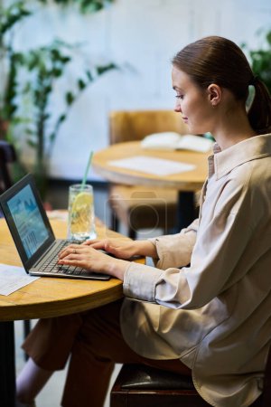 Photo for Young brunette businesswoman in quiet luxury attire sitting by table in front of laptop, typing and analyzing online financial data - Royalty Free Image