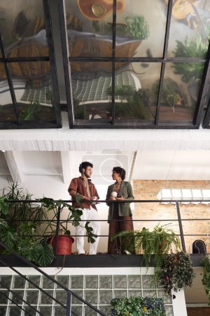 Téléchargez les photos : Sous l'angle de deux jeunes employés ou amis avec café bavarder tout en se tenant par la main courante dans un café décoré de plantes vertes - en image libre de droit