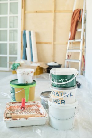 Photo for Two stacks of plastic buckets containing paints for walls and paintroller in tray standing on the floor of living room in new apartment - Royalty Free Image