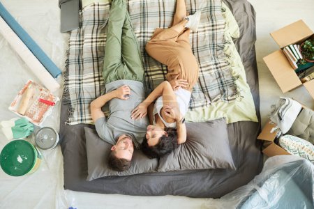 Téléchargez les photos : Vue ci-dessus du jeune couple affectueux couché sur un carreau à carreaux sur le sol du salon tout en profitant du repos après le déménagement ou la rénovation - en image libre de droit