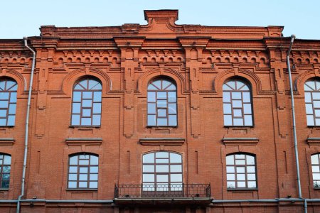 Foto de Parte superior del antiguo edificio histórico de ladrillo rojo con un grupo de ventanas en el entorno urbano contra el cielo azul - Imagen libre de derechos