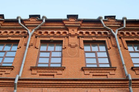 Téléchargez les photos : Partie du bâtiment historique en brique rouge avec fenêtres et tuyaux de gouttière sur la façade debout devant la caméra avec ciel bleu au-dessus - en image libre de droit