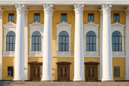 Photo for Front part of munucipal or cultural institution with white plaster columns, row of long arch shaped windows, wooden doors and yellow walls - Royalty Free Image