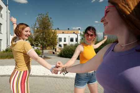 Téléchargez les photos : Heureuses petites amies mignonnes en tenue décontractée faisant pile de mains et s'amusant tout en profitant de se promener sur des patins à roulettes en milieu urbain en été - en image libre de droit