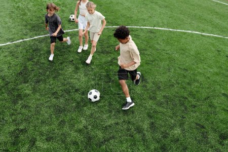 Photo for Above angle of several schoolchildren playing soccer on green football field at stadium while three of them running after ball during game - Royalty Free Image