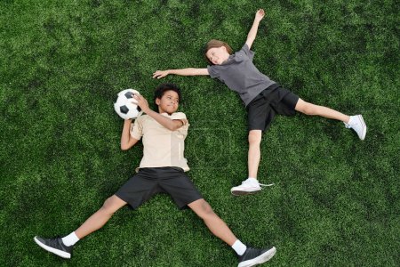 Foto de Vista superior de dos jugadores de fútbol intercultural feliz con pelota acostado en el césped verde o campo de fútbol y jugar su juego de deportes favoritos en el ocio - Imagen libre de derechos