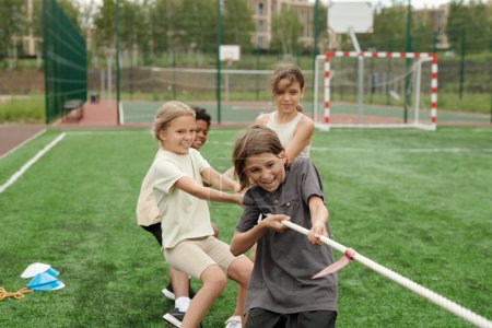Photo for Group of strong and active schoolchildren making effort while pulling rope during school sports competition with more powerful team at stadium - Royalty Free Image