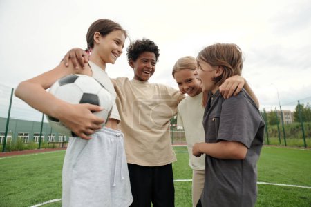 Photo for Four laughing intercultural friends standing in front of each other after game of soccer and having chat while enjoying rest after play - Royalty Free Image