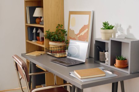 Arbeitsplatz des Home Office Managers mit Laptop umgeben von heimischen Pflanzen, dekorativen Figuren, Bild für Bild, Ordner und Notizbuch