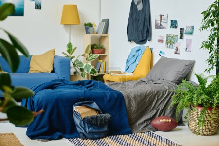 Foto de Parte de un amplio dormitorio o sala de estar con cómoda cama doble con manta azul y sofá con cojines de pie junto a las paredes con carteles - Imagen libre de derechos