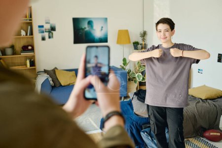 Foto de Sonriente adolescente mostrando ejercicio de baile mientras mira la cámara del teléfono inteligente en poder de su novio disparando video para suscriptores - Imagen libre de derechos