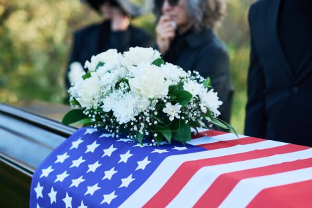Ein Bündel frischer weißer Rosen und Chrysanthemen auf dem mit amerikanischer Flagge bedeckten Sarg während der Trauerfeier für den verstorbenen Veteranen