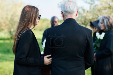 Téléchargez les photos : Vue de dos de la jeune femme en tenue noire soutenant un homme mûr aux cheveux blancs lors des funérailles de leur parent, ami ou membre de la famille - en image libre de droit