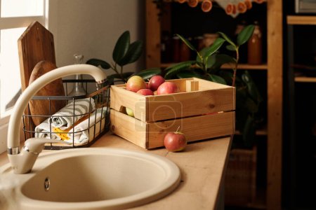 Foto de Grifo y lavabo metálico beige en el mostrador de la cocina con caja de madera de manzanas maduras cultivadas en el jardín por casa de campo o casa de campo en otoño - Imagen libre de derechos