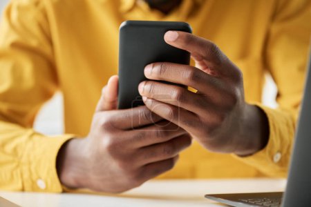 Téléchargez les photos : Focus sur les mains de jeunes cols blancs afro-américains tenant smartphone et textos assis sur le lieu de travail au bureau - en image libre de droit
