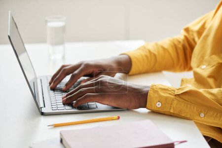 Foto de Manos de joven empleado afroamericano en camisa amarilla tocando las teclas del teclado del ordenador portátil durante el trabajo sobre el nuevo proyecto empresarial en la oficina - Imagen libre de derechos
