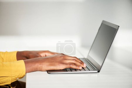 Téléchargez les photos : Vue latérale des mains du jeune employé masculin tapant sur le clavier de l'ordinateur portable assis par le bureau devant la caméra et travaillant sur un nouveau projet - en image libre de droit