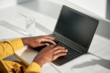 Téléchargez les photos : Mains de jeunes étudiants afro-américains de sexe masculin ou cols blancs touchant les touches du clavier de l'ordinateur portable tout en étant assis par bureau dans le bureau - en image libre de droit