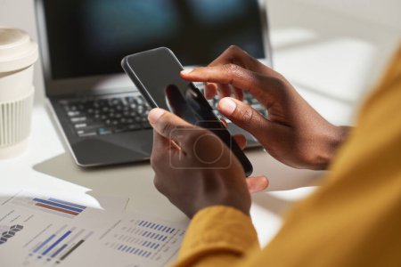Photo for Hands of African American male economist pointing at screen of smartphone while sitting by desk in front of laptop and working with data - Royalty Free Image