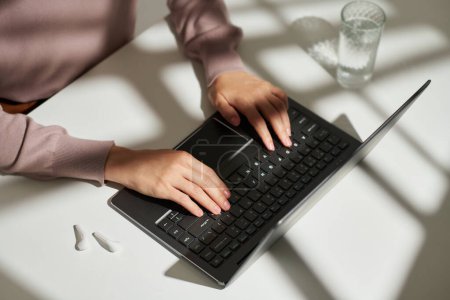 Téléchargez les photos : Au-dessus de l'angle des mains de la jeune étudiante ou solpreneur appuyant sur les touches du clavier d'ordinateur sans fil tout en étant assis près de son lieu de travail - en image libre de droit