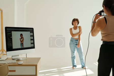Photo for Rear view of young female photographer taking pictures of fashion model while standing by computer screen with shots of young woman - Royalty Free Image