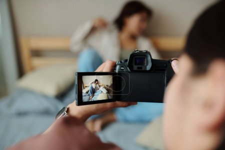 Photo for Focus on screen of photocamera held by photographer taking pictures of female fashion model relaxing on double bed during photo shooting - Royalty Free Image