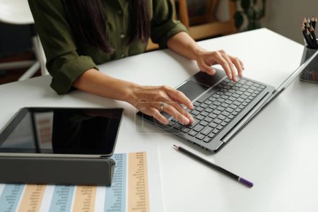 Téléchargez les photos : Mains de l'enseignant tapant sur le clavier de l'ordinateur portable tout en étant assis à côté du bureau avec tablette et document avec les règles de grammaire et de consulter les étudiants en ligne - en image libre de droit